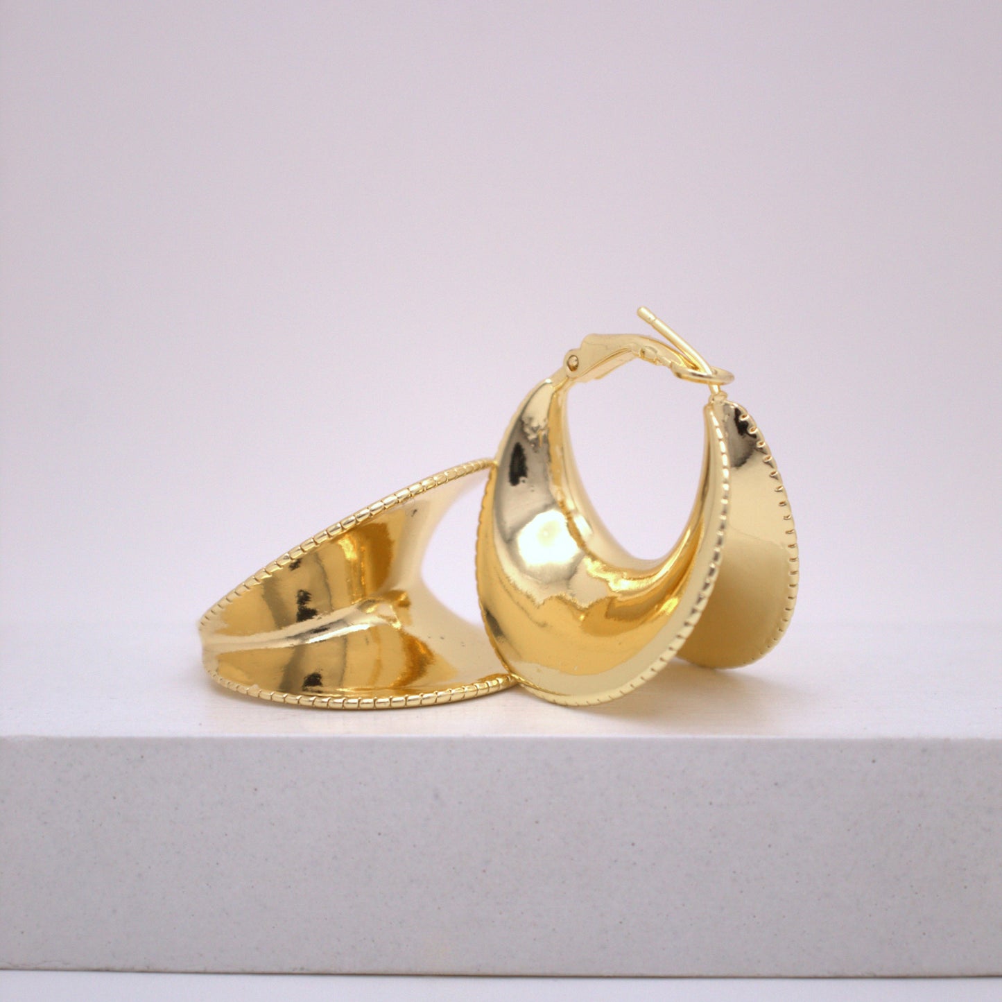 Gold hoop earrings on a white surface with a light gray background