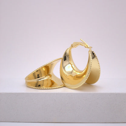 Gold hoop earrings on a white surface with a light gray background