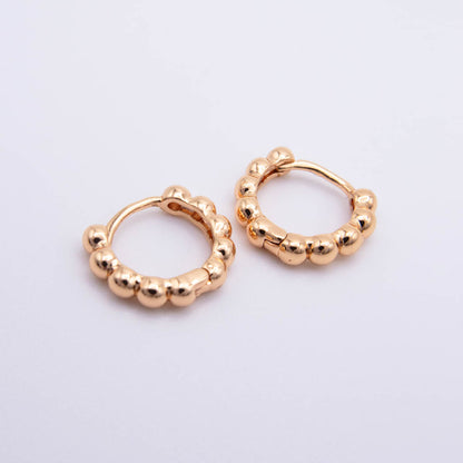 A pair of small gold huggie hoop earrings with a textured, beaded outer edge, displayed on a clean white background.