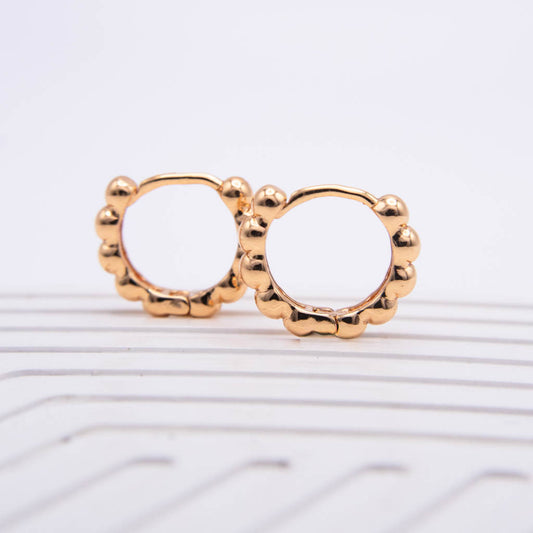 A pair of gold-toned hoop earrings with a scalloped, beaded border, displayed on a white ribbed surface against a white background.