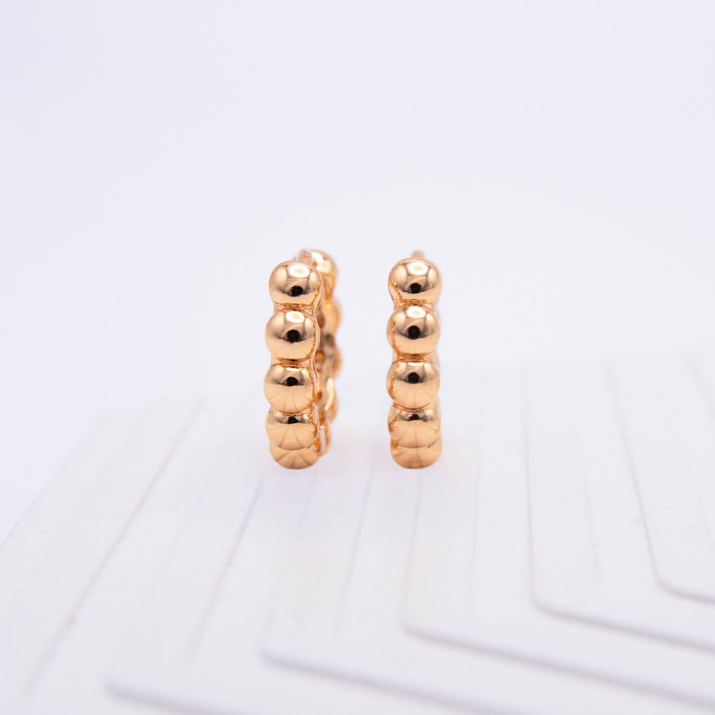 A pair of small gold hoop earrings with a textured, beaded vertical design, standing upright on a white surface.