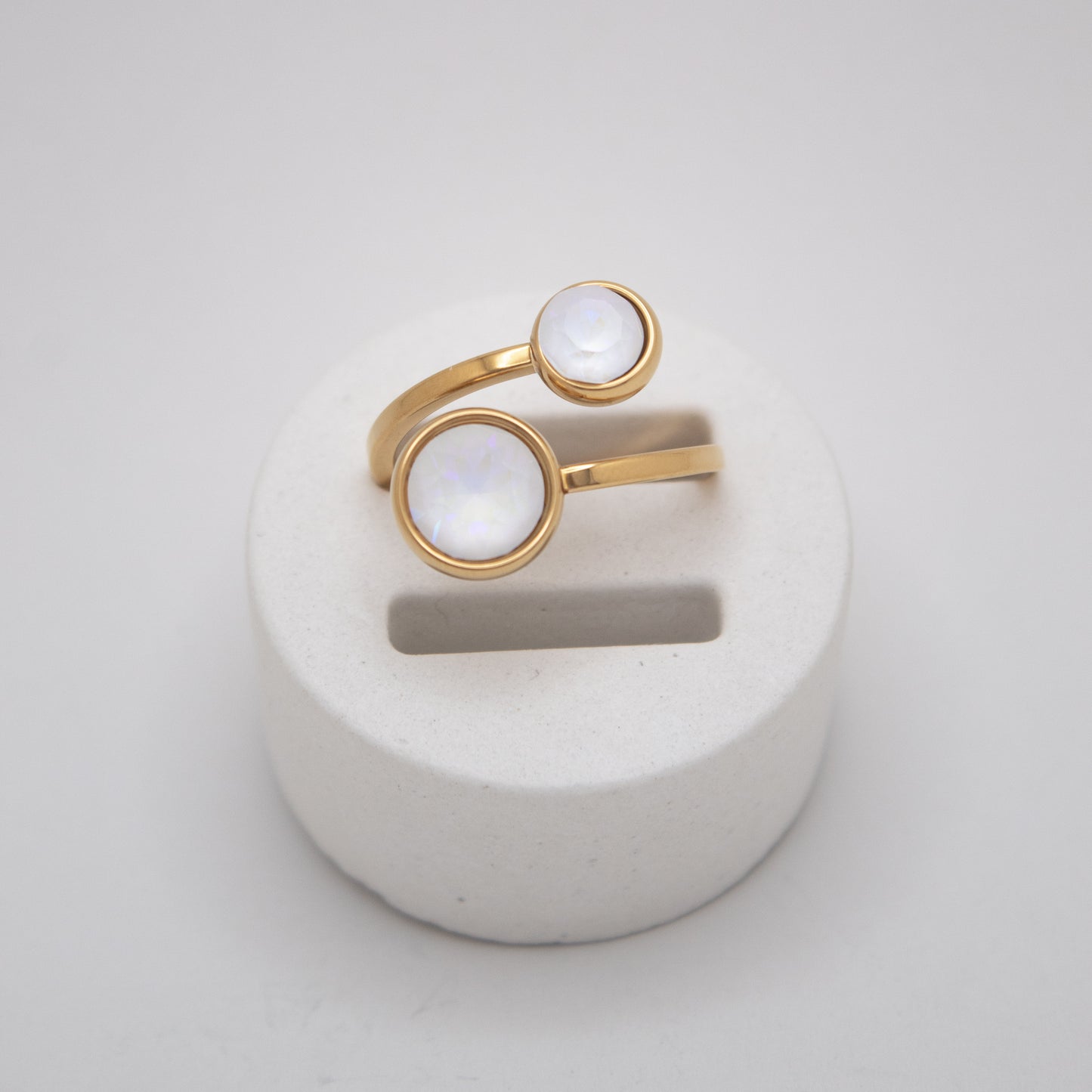 Gold ring with white stones on a white stand against a light gray background