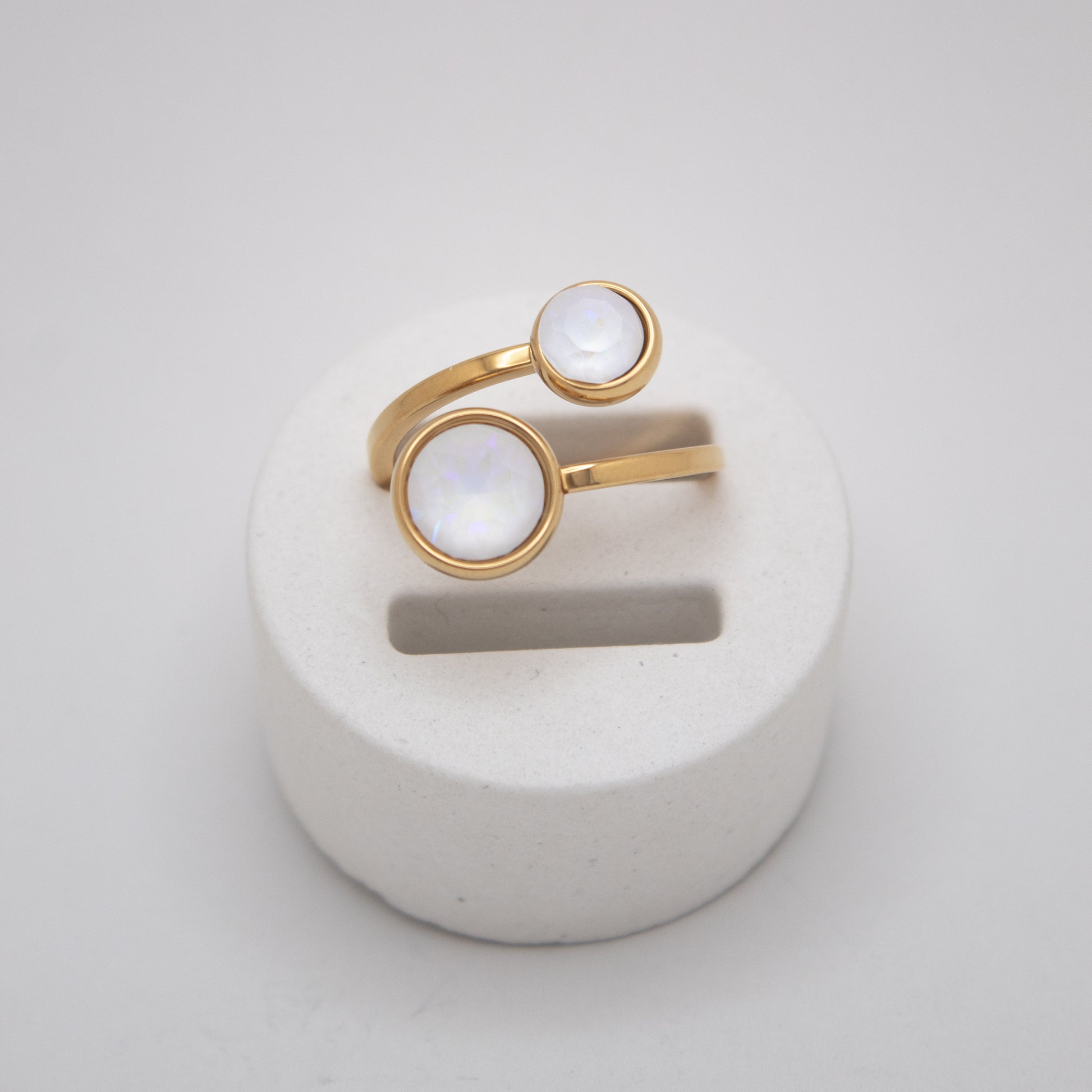 Gold ring with white stones on a white stand against a light gray background