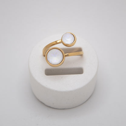Gold ring with white stones on a white stand against a light gray background
