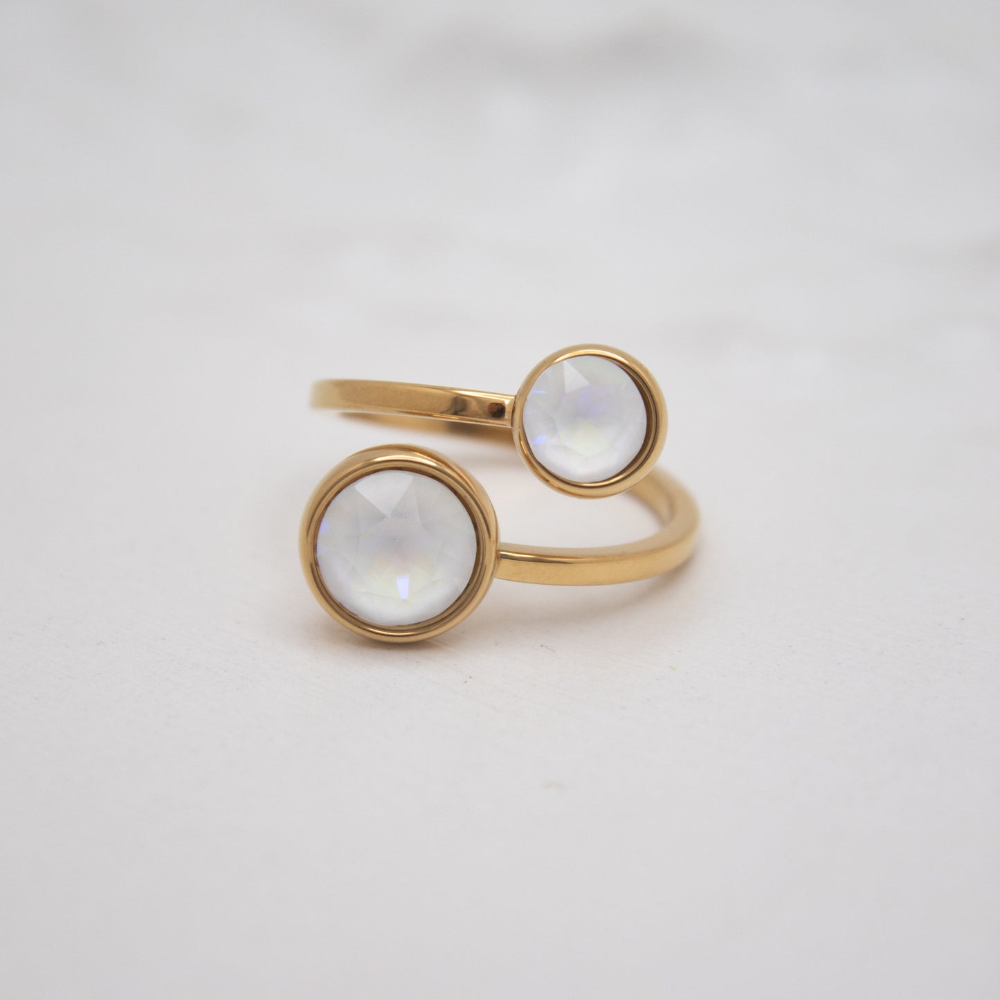 Gold ring with two circular white gemstones on a light gray background