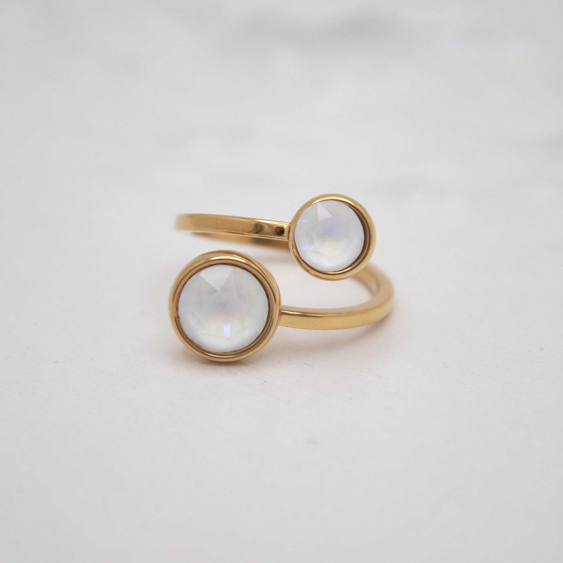 Gold ring with two circular white gemstones on a light gray background