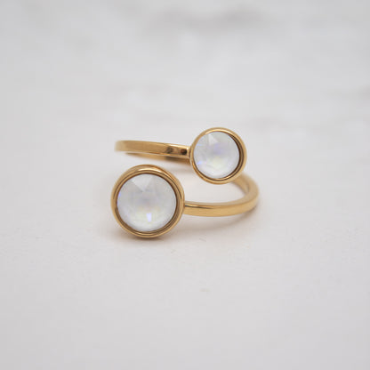 Gold ring with two circular white gemstones on a light gray background