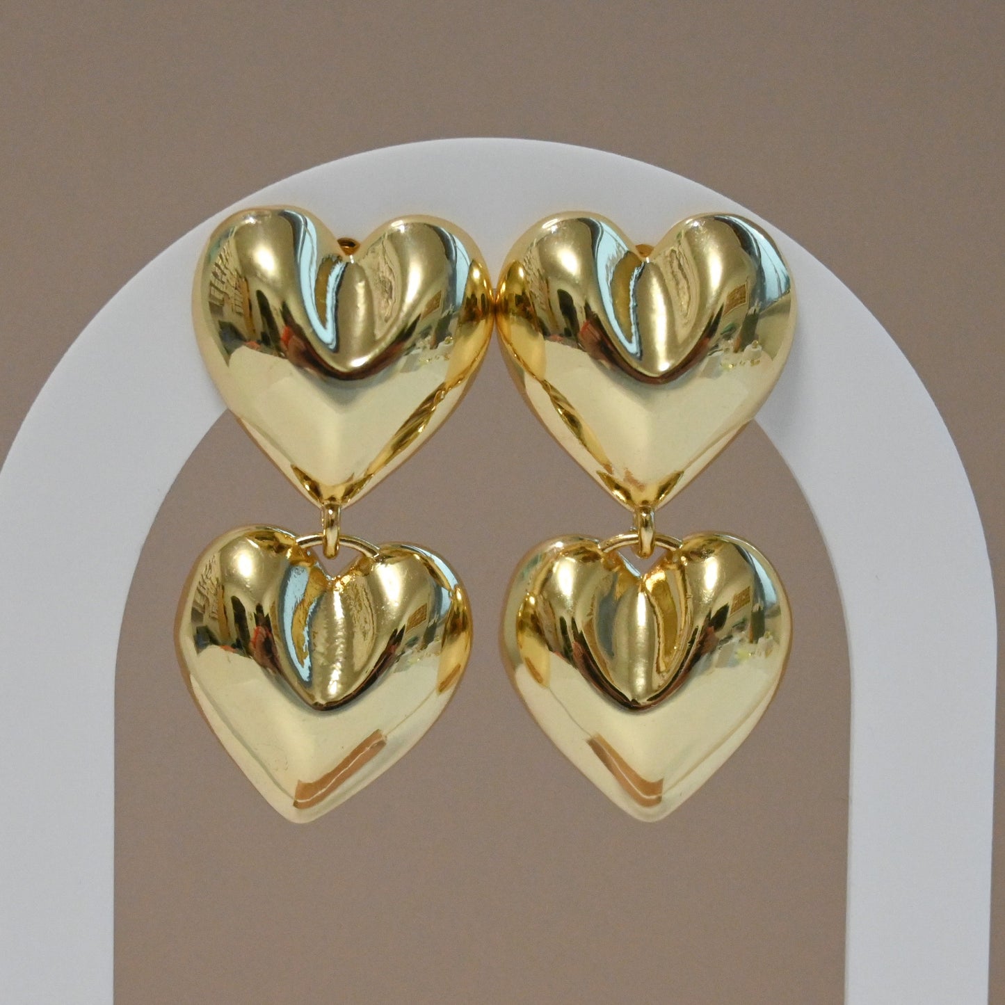 A pair of gold-colored double heart-shaped stud earrings hanging from a white metal stud base.