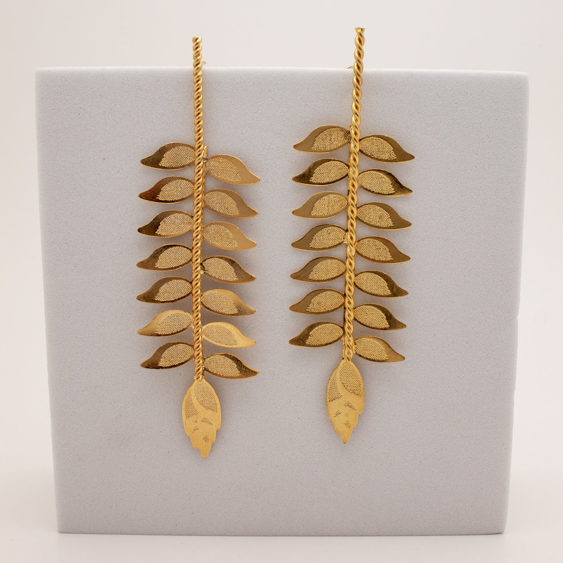 Pair of gold leaf-shaped earrings on a gray display card.