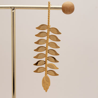 Gold leaf-shaped earring on a stand with a neutral background