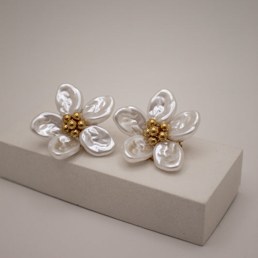 Pair of floral earrings with pearl-like petals and gold centers on a beige stand.