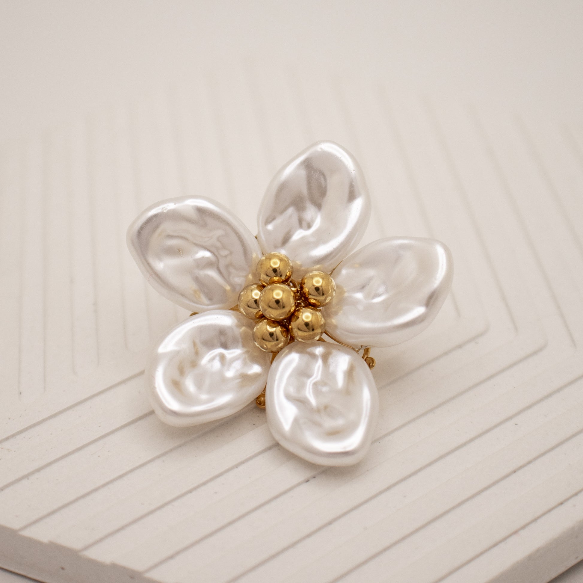 Pearl flower brooch with gold center on a white background