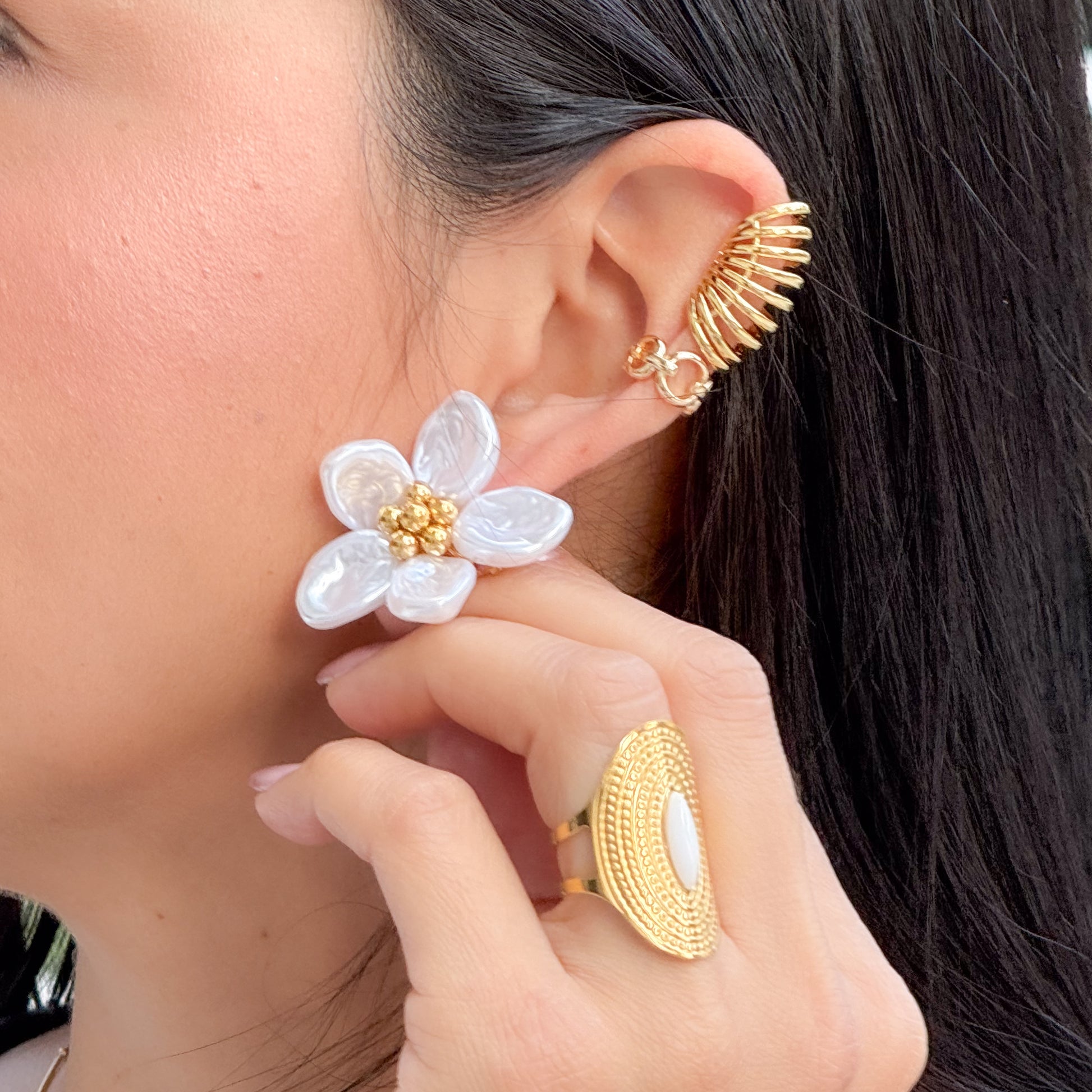Close-up of a person wearing gold and white floral earrings with matching rings.