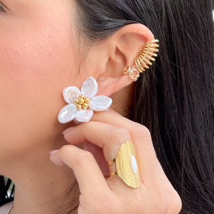Close-up of a person wearing gold and white floral earrings with matching rings.