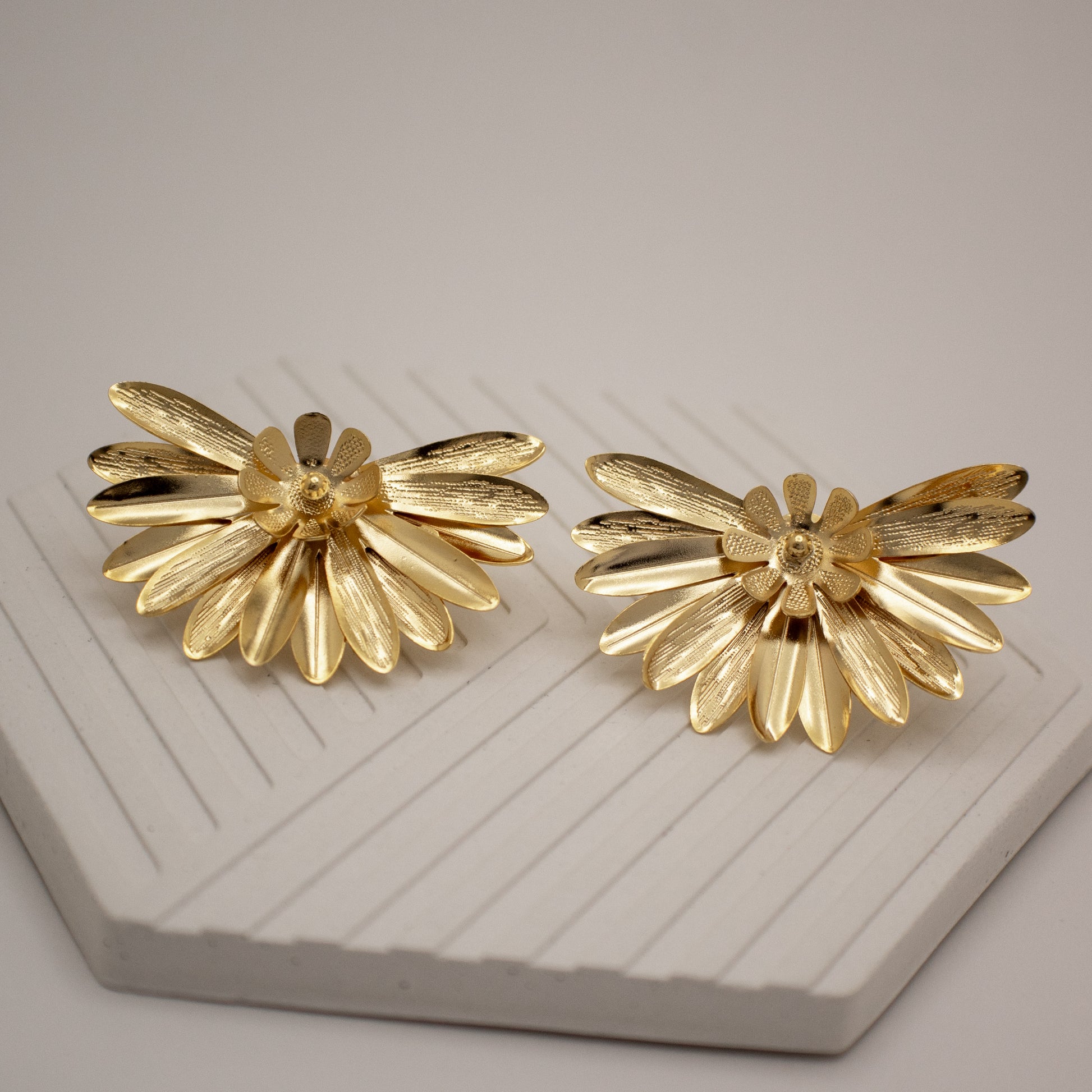 Pair of gold flower-shaped earrings on a textured surface