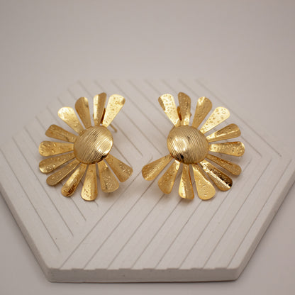 Pair of gold floral earrings on a white textured surface