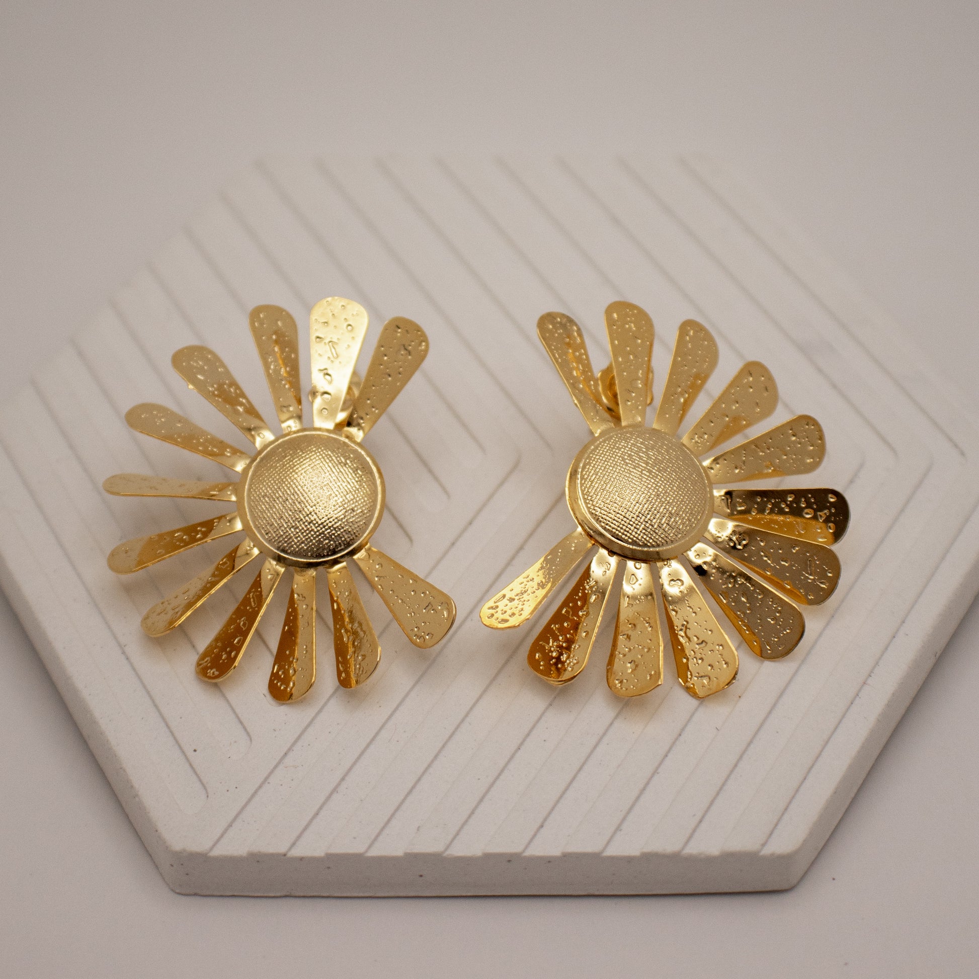 Pair of gold sunflower-shaped earrings on a textured white surface
