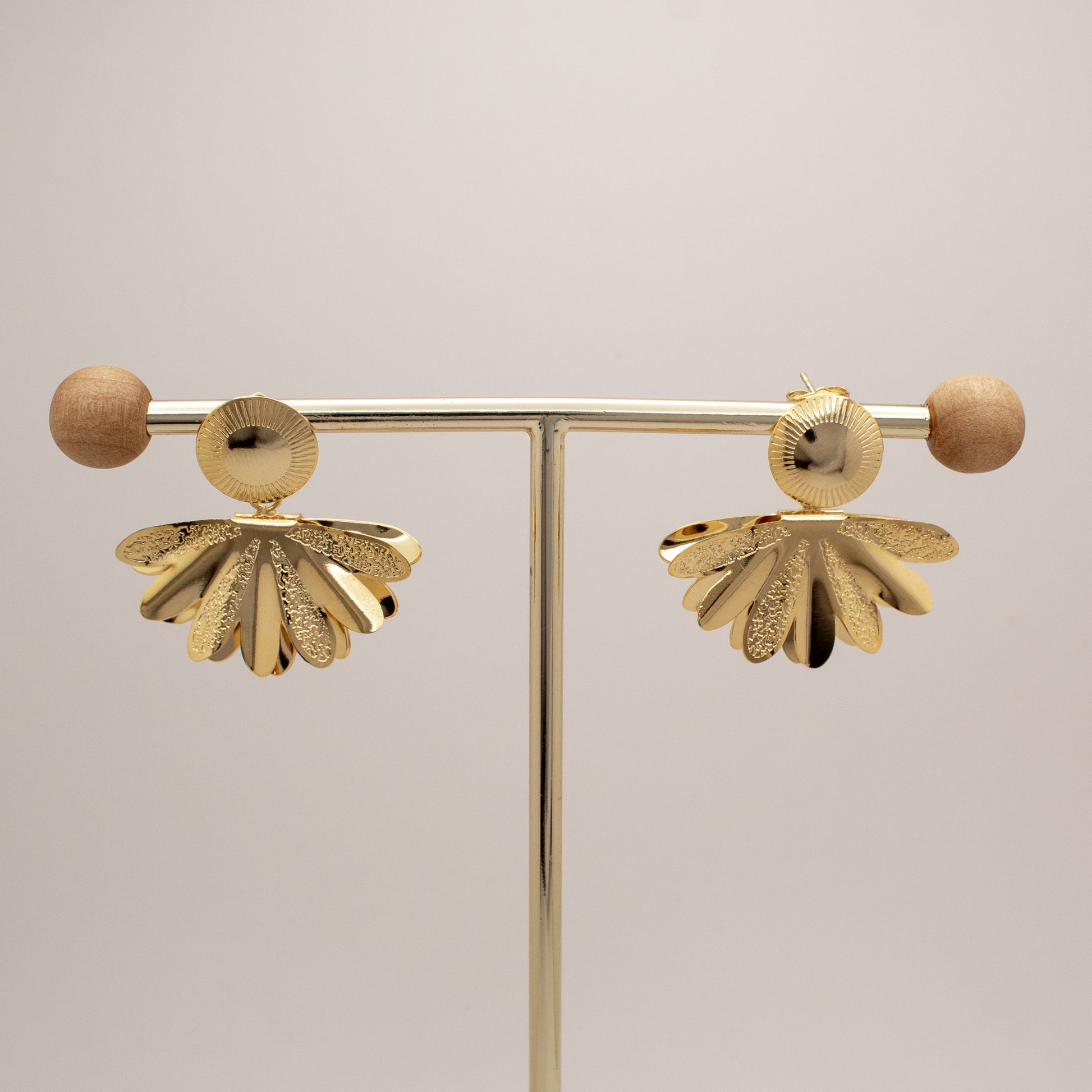 Pair of gold earrings on a stand against a light background