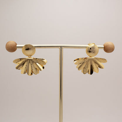 Pair of gold earrings on a stand against a light background