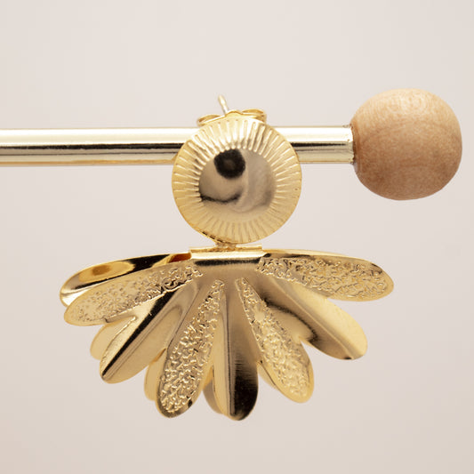 Gold earring with a textured design on a light gray background