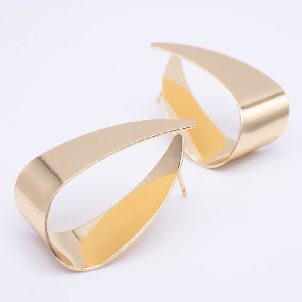 A pair of abstract, open teardrop-shaped earrings in polished yellow gold, photographed on a clean white background.