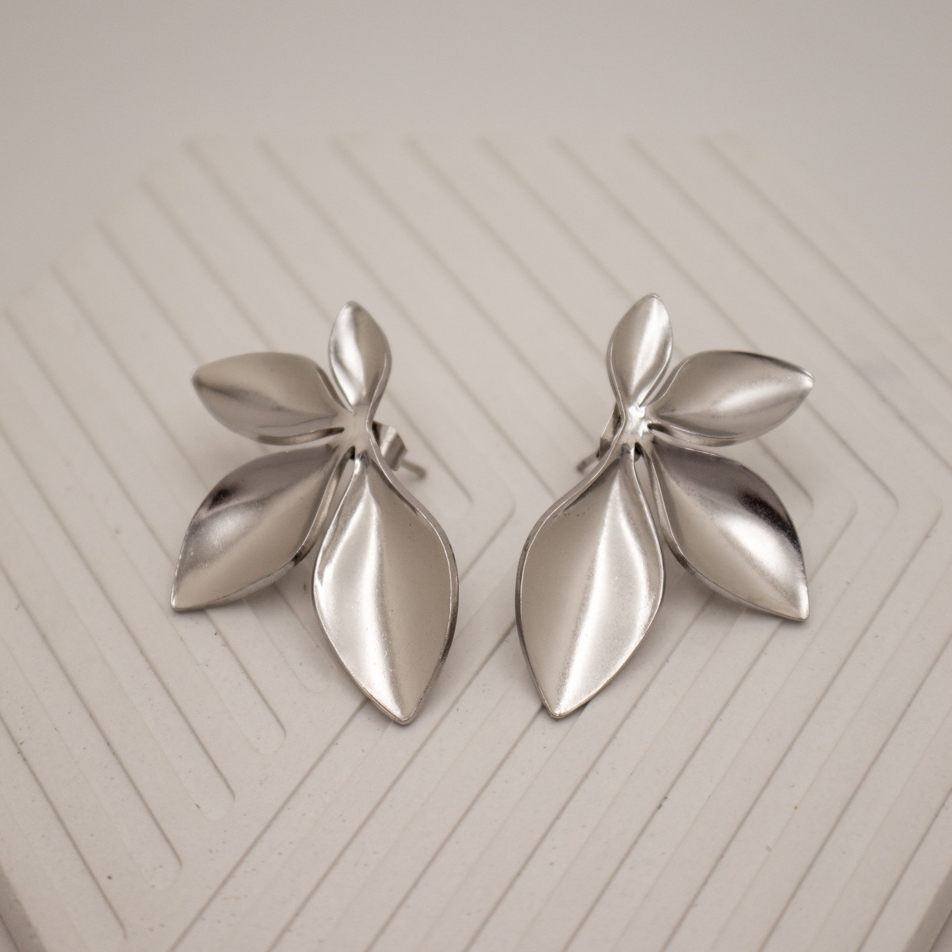 Pair of silver leaf-shaped earrings on a light wooden surface