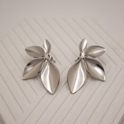 Pair of silver leaf-shaped earrings on a light wooden surface