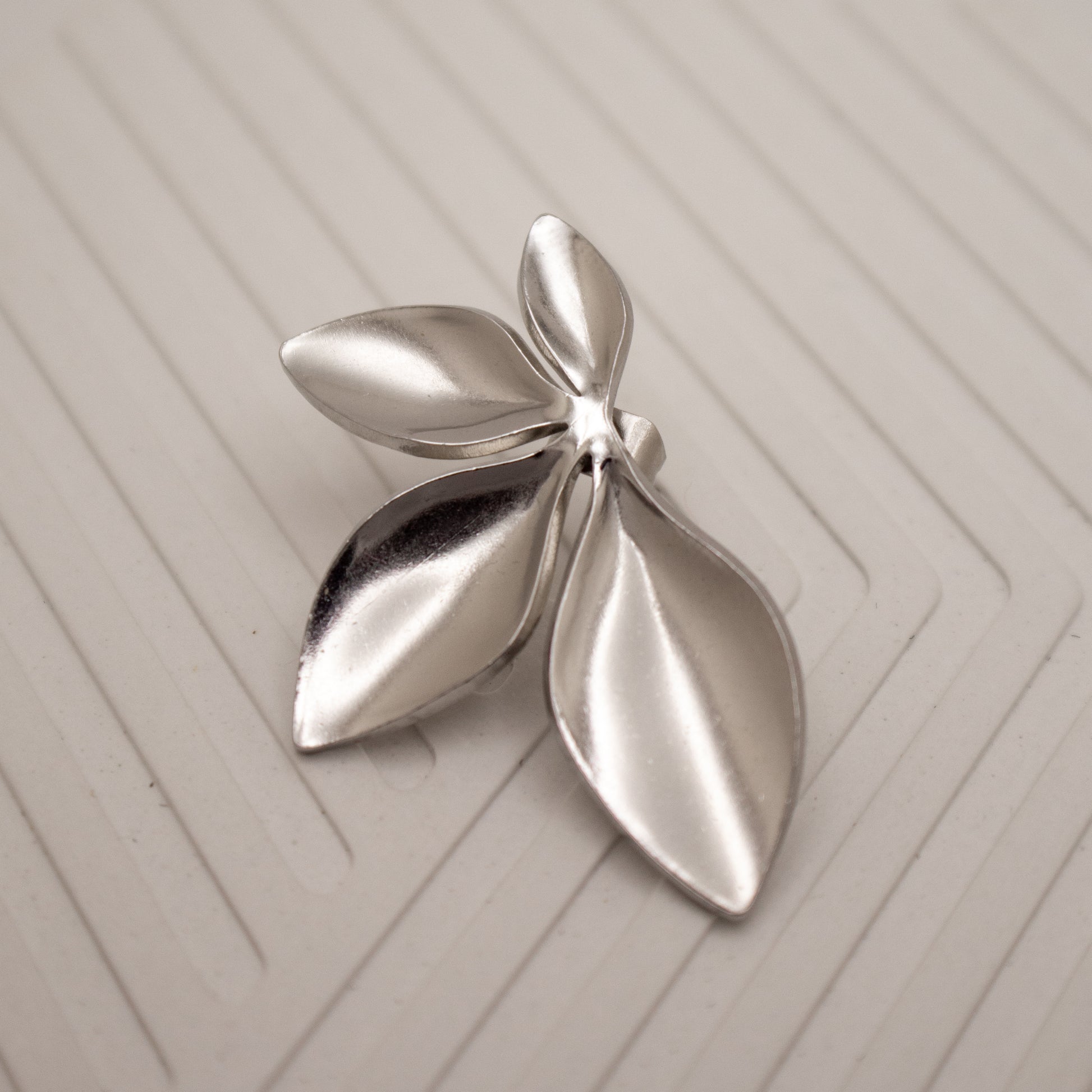 Silver leaf-shaped brooch on a textured beige surface
