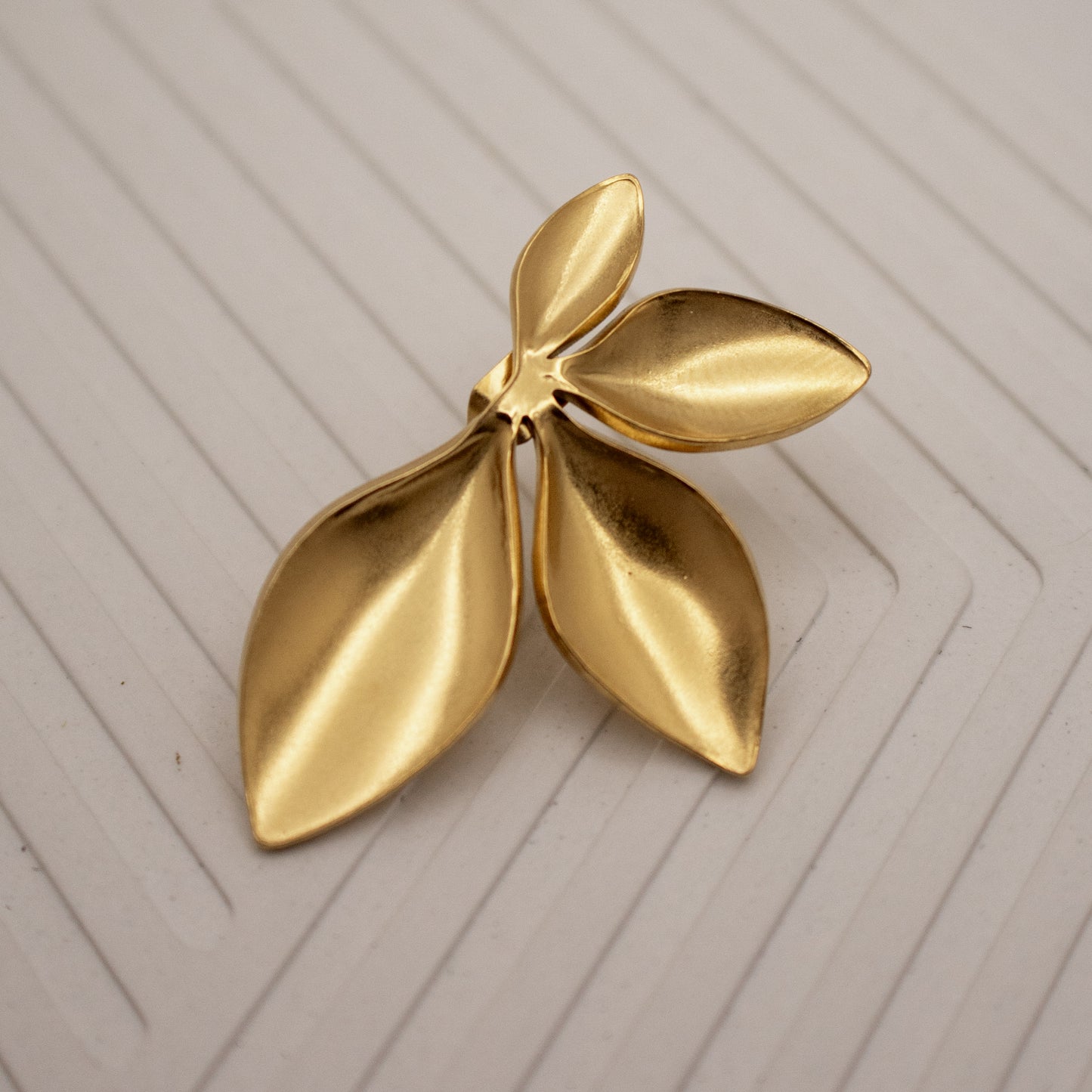 Gold leaf-shaped brooch on a textured beige background
