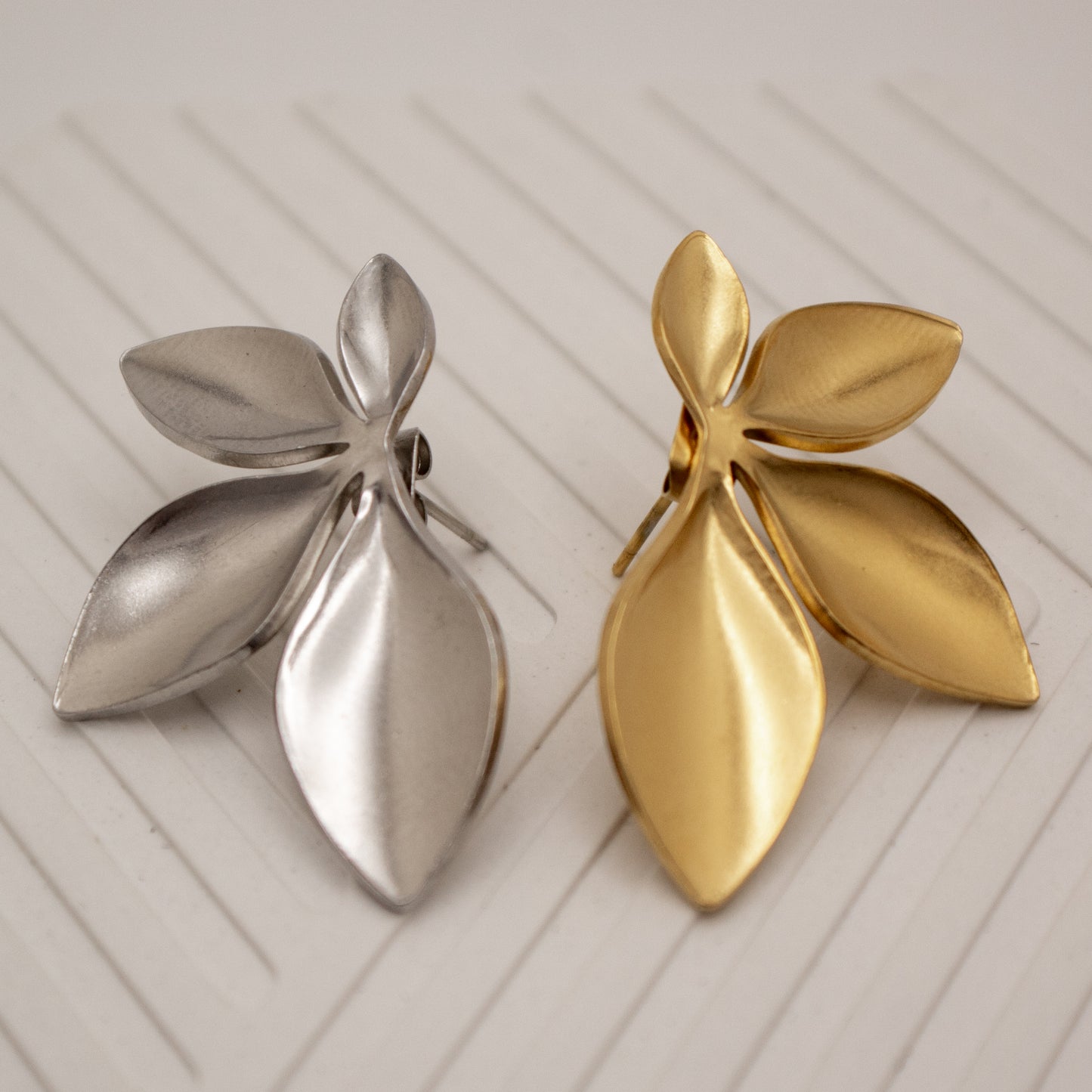 Gold and silver leaf-shaped earrings on a light wooden surface