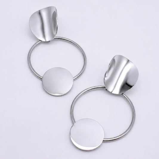 A pair of modern silver-toned statement earrings featuring a circular ring, a flat round disc, and a curved leaf-like top piece, displayed on a clean white background.