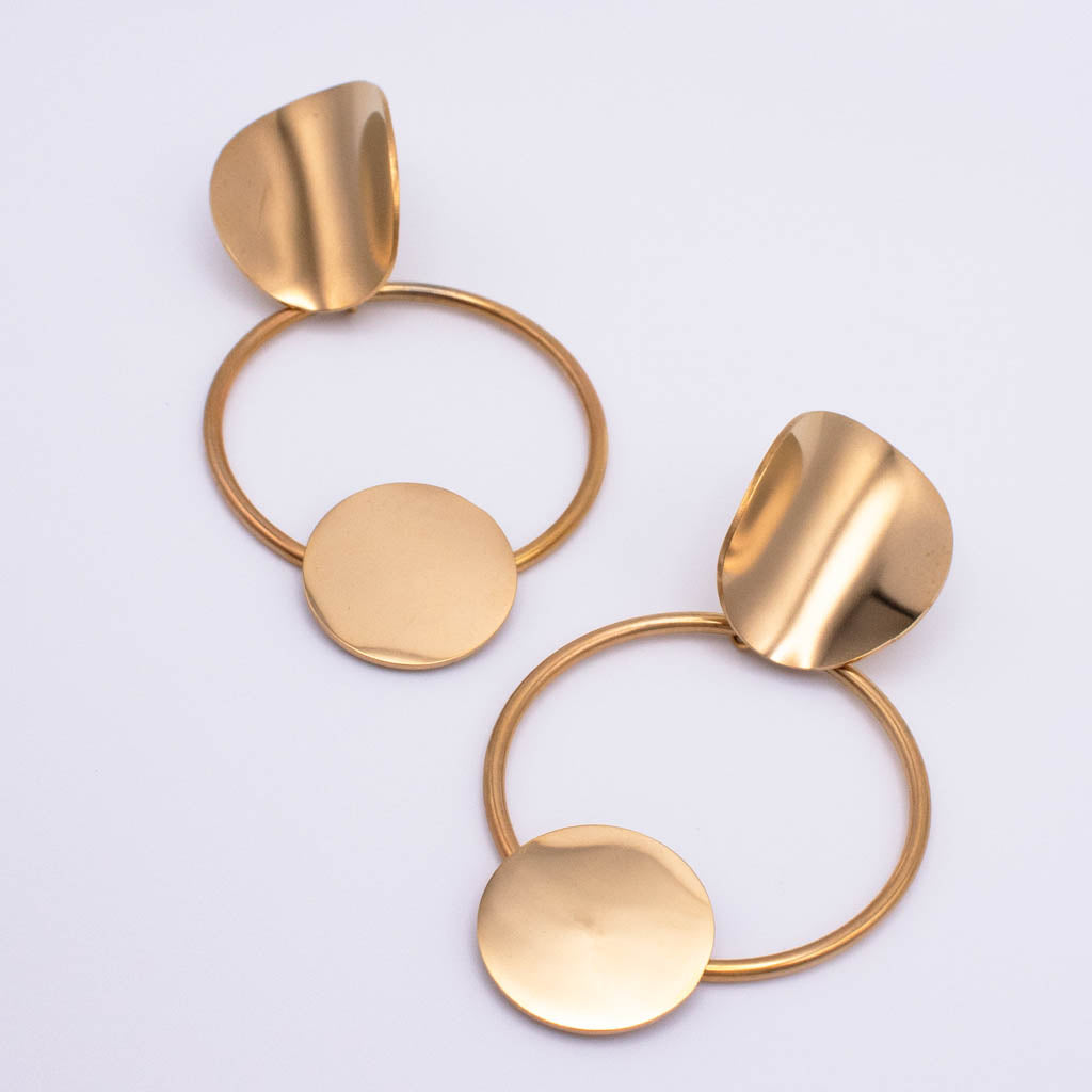 A pair of modern gold-toned dangle earrings with circular hoops, flat round discs, and organic leaf-like top pieces, photographed on a clean white background.