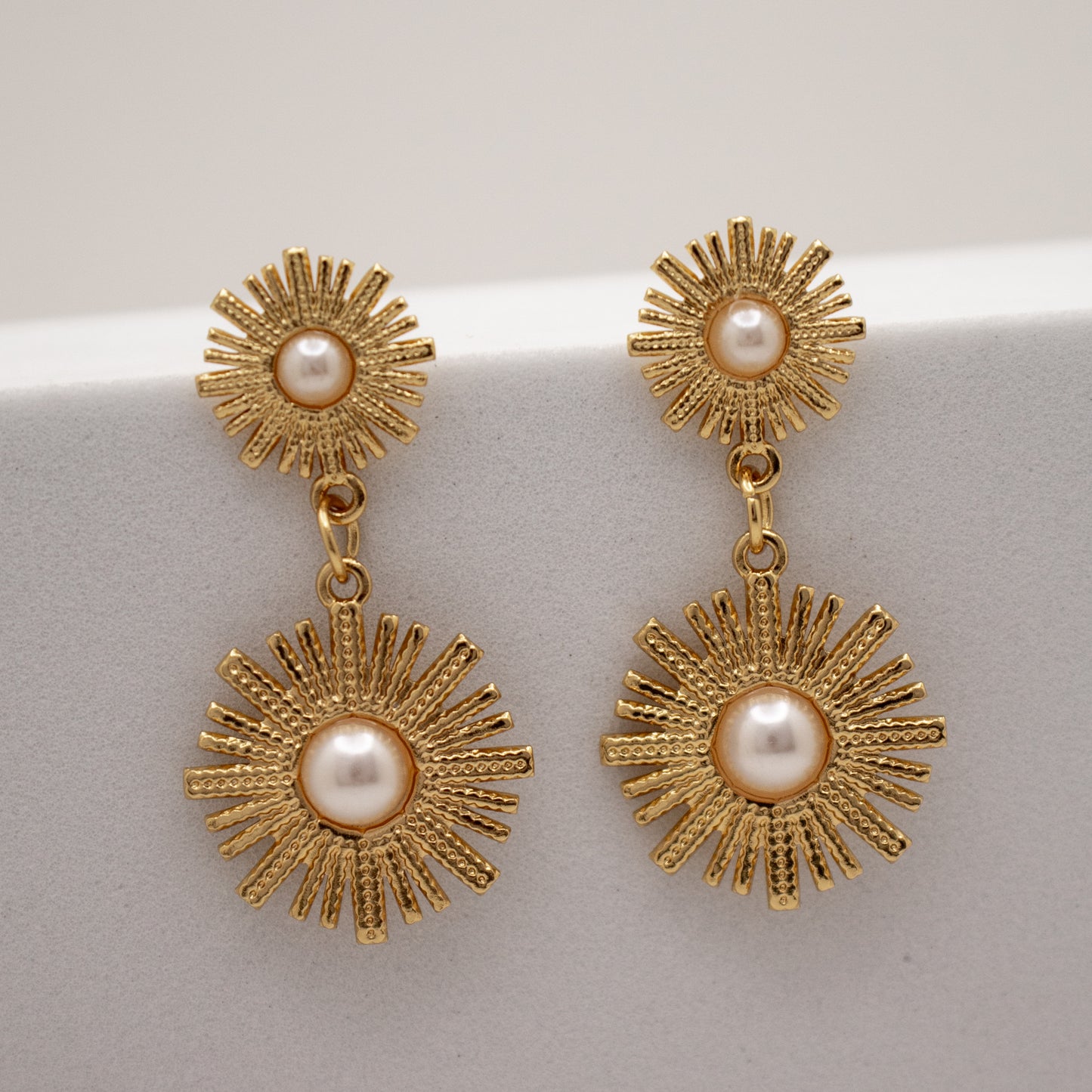 Gold dandelion earrings with pearl centers on a light gray background