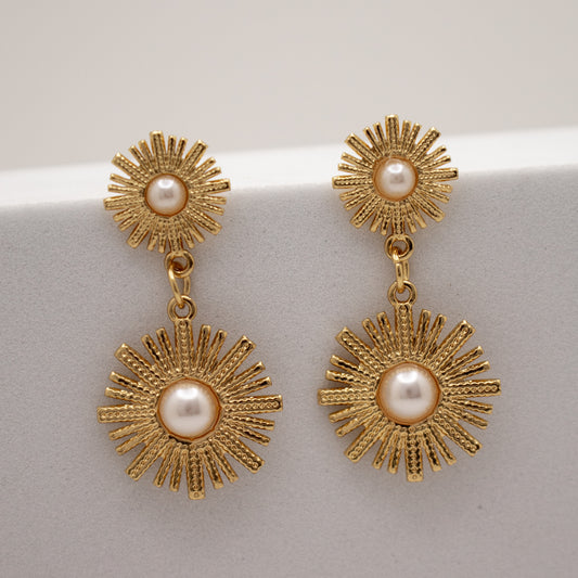 Gold dandelion earrings with pearl centers on a light gray background
