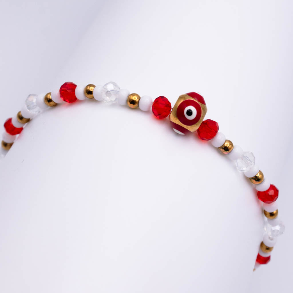 A beaded bracelet with red faceted beads, clear glass beads, small gold spacer beads, and a central gold hexagonal evil eye charm, displayed on a white background.