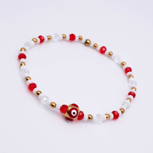 A beaded stretch bracelet featuring red faceted beads, clear crystal beads, small gold metal beads, and a central gold evil eye charm with red and white details, photographed on a clean white background.