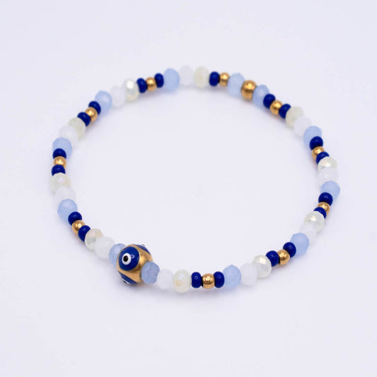 A beaded stretch bracelet featuring light blue, white, and dark blue beads, accented with small gold spacer beads and a central blue and white evil eye charm, shown on a plain white background.