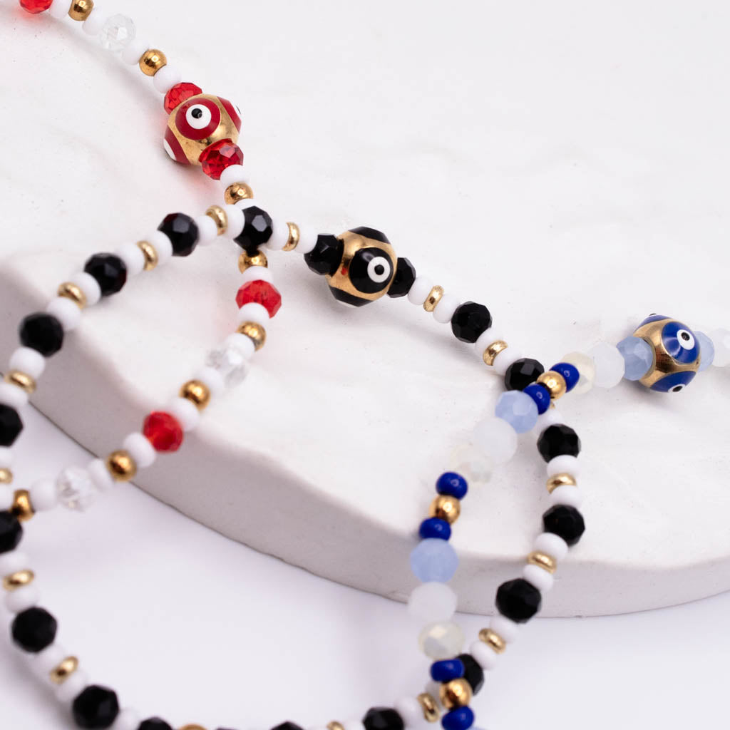 A close-up of a beaded bracelets featuring evil eye charms and multi-colored beads, including red, black, white, blue, and gold, arranged on a white textured surface.