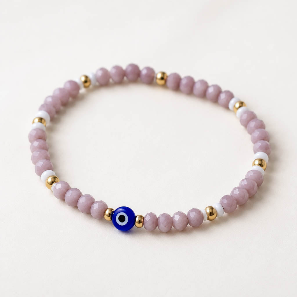 A beaded stretch bracelet with light purple faceted beads, white beads, gold spacer beads, and a blue evil eye charm.