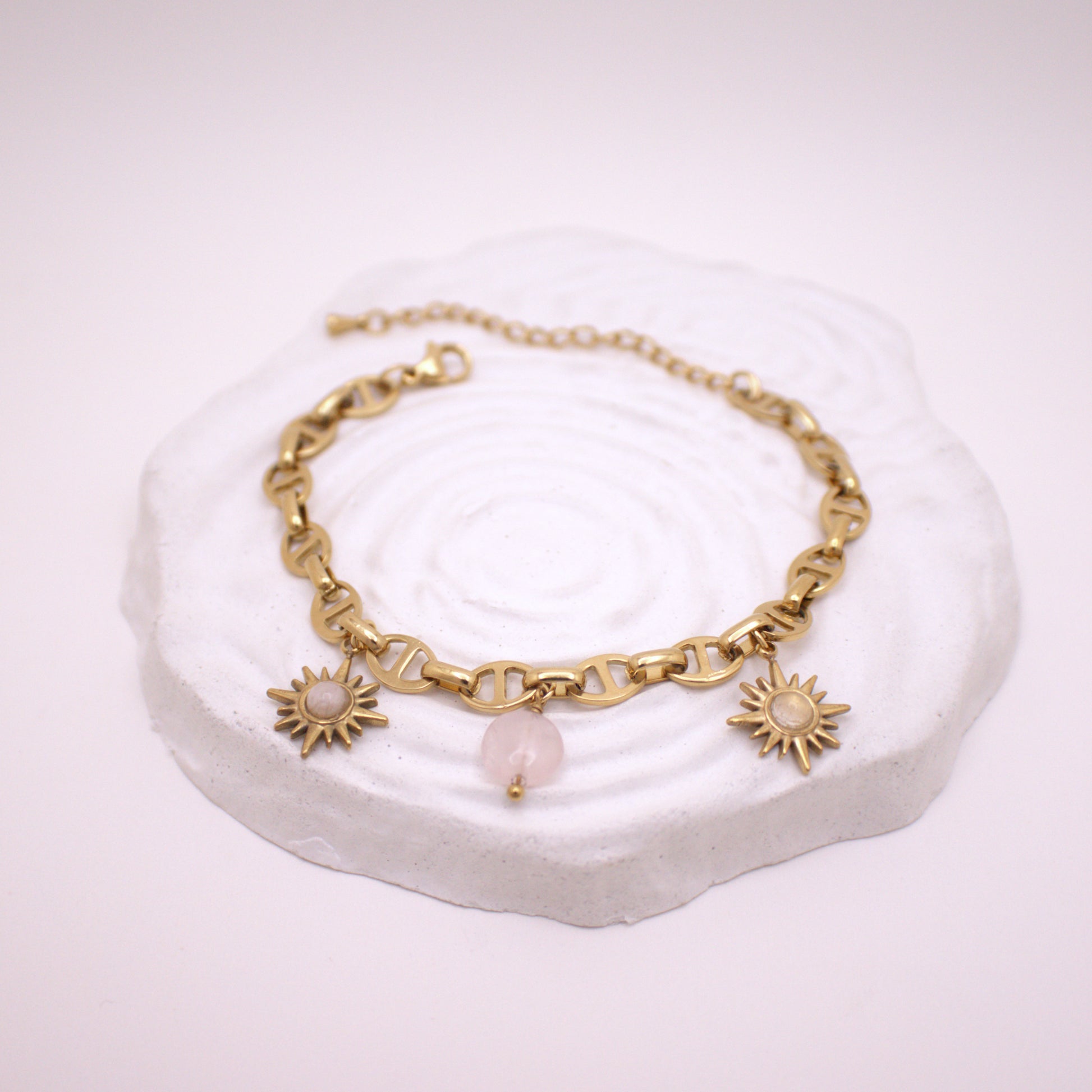 Gold bracelet with sun-shaped charms on a white stone surface