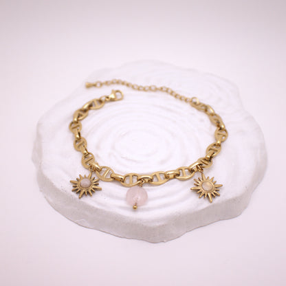 Gold bracelet with sun-shaped charms on a white stone surface