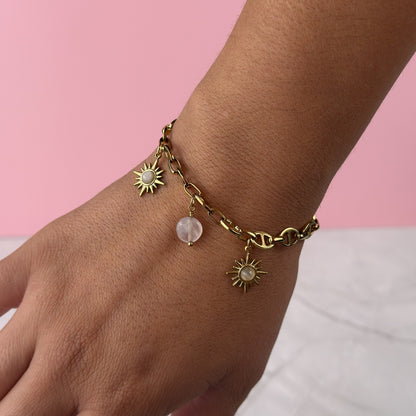 Gold bracelet with sun and moon charms on a wrist against a pink background