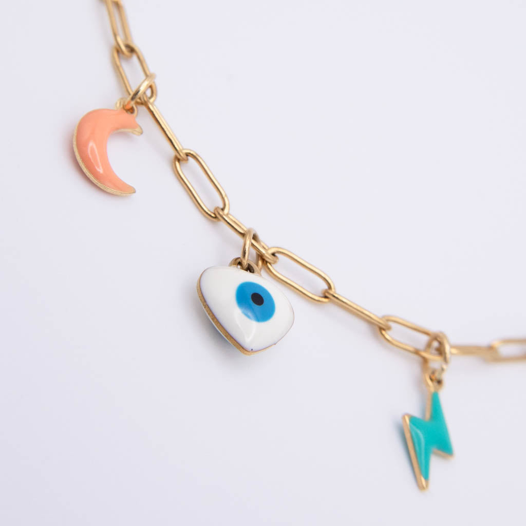 Gold paperclip chain bracelet with three charms: a peach crescent moon, a white evil eye pendant, and a turquoise lightning bolt, on a white background.