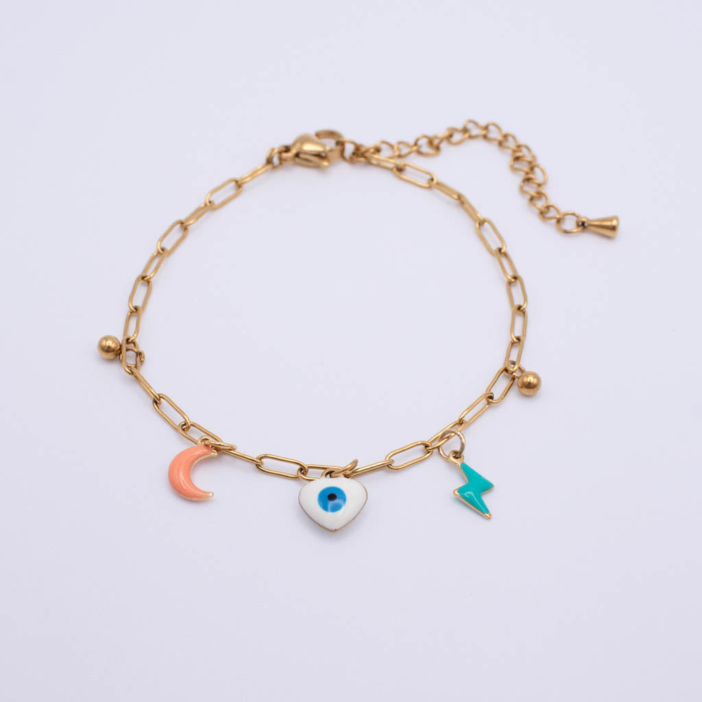 A gold paperclip chain bracelet with three charms: a peach crescent moon, a white heart with a blue evil eye, and a teal lightning bolt, shown on a light gray background.