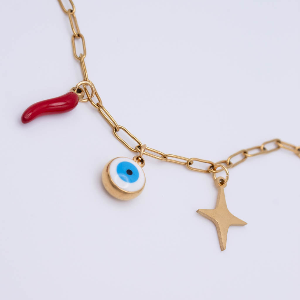 Gold paperclip chain necklace with three charms: a red italian horn, a gold evil eye pendant, and a gold star, on a light gray background.