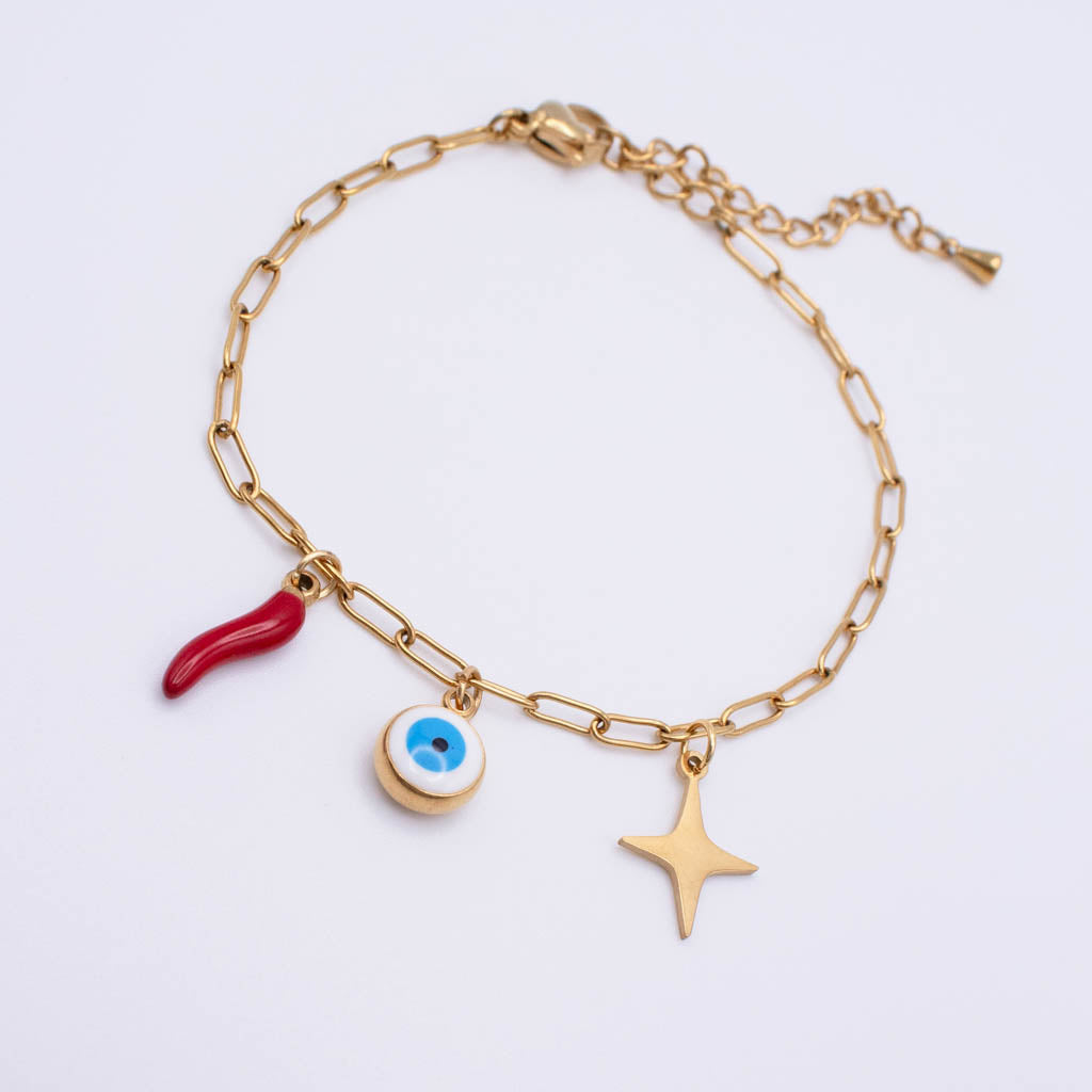 A gold paperclip chain bracelet featuring three charms: a red italian horn an evil eye pendant, and a gold star, displayed on a clean white background.