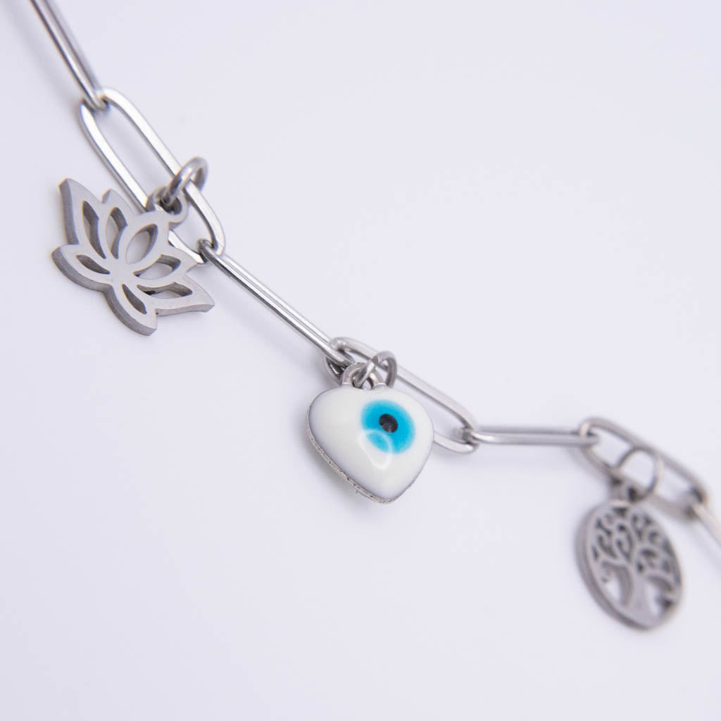 A silver-tone charm bracelet featuring a lotus flower, an evil eye heart, and a tree of life pendant, shown on a clean white background.