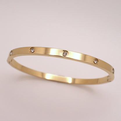 Gold bracelet with embedded diamonds on a light beige background