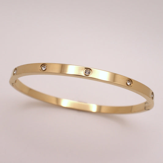 Gold bracelet with embedded diamonds on a light beige background