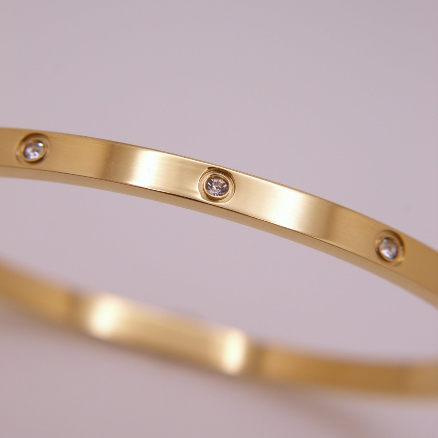 Gold bracelet with embedded diamonds on a light gray background